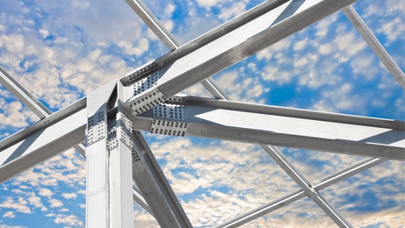 Close-up of a metal framework with beams and rivets, shown against a cloudy blue sky.