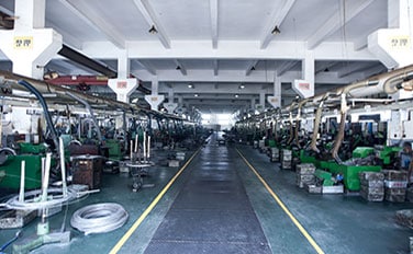 Floresan ışıkların altında, merkezi koridorun her iki tarafında yeşil makinelerin sıralandığı fabrika.