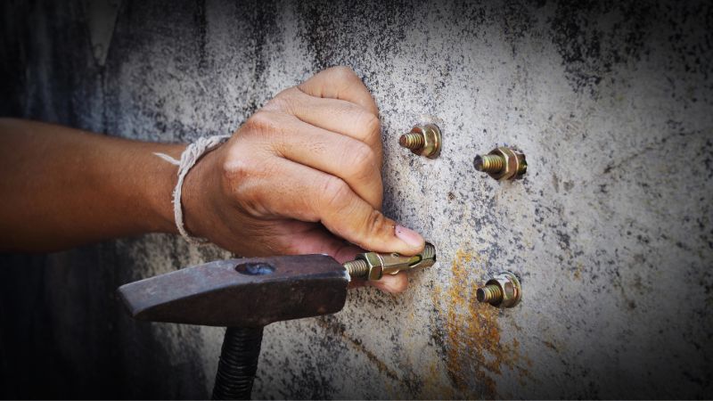 Bir kişi bir anahtar yardımıyla beton duvara bir manşon dübeli yerleştirir; yakınlarda birkaç cıvata zaten takılmıştır.