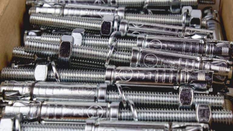 Metal wedge and sleeve anchor bolts with nuts, close-up, arranged inside a cardboard box.