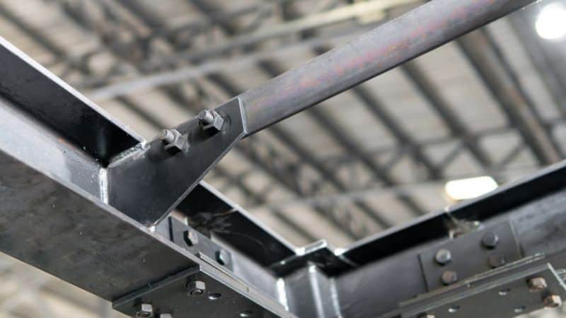 Close-up of a metal framework with bolted joints and hex nuts on angled beams against an industrial ceiling.