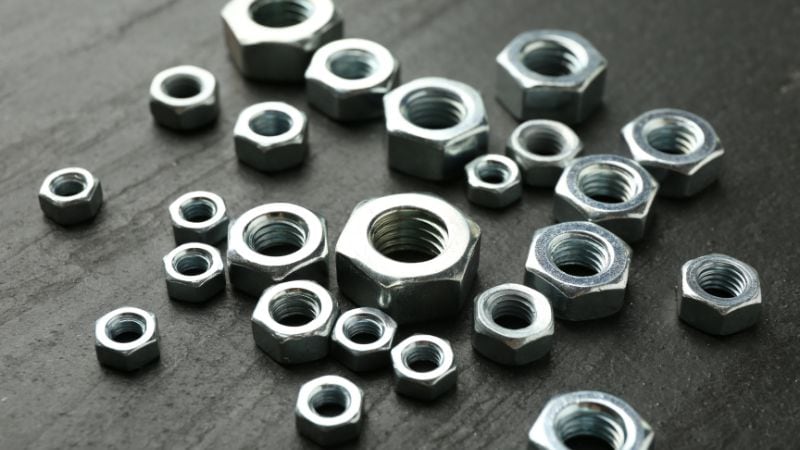 Hex nuts of various sizes are scattered on a dark, textured surface.